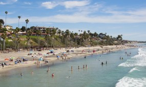 A shot from the San Clemente Pier shows the water full of swimmers, a beautiful blue sky, and the coastal bluffs.