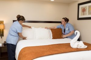 Two housekeepers fluff the pillows on a full-size bed