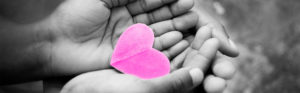 black and white photo of hands holding pink paper heart