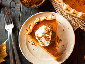 slice of pumpkin pie with whipped cream and full pie and forks