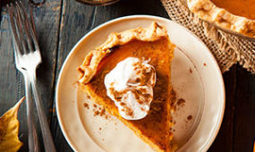 slice of pumpkin pie with whipped cream and full pie and forks