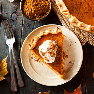 slice of pumpkin pie with whipped cream and full pie and forks