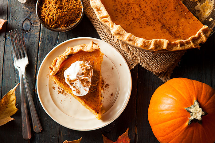 slice of pumpkin pie with whipped cream and full pie and forks